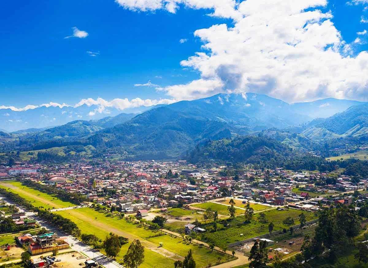 Ciudad en un valle verde entre montañas, con campos y una avenida arbolada
