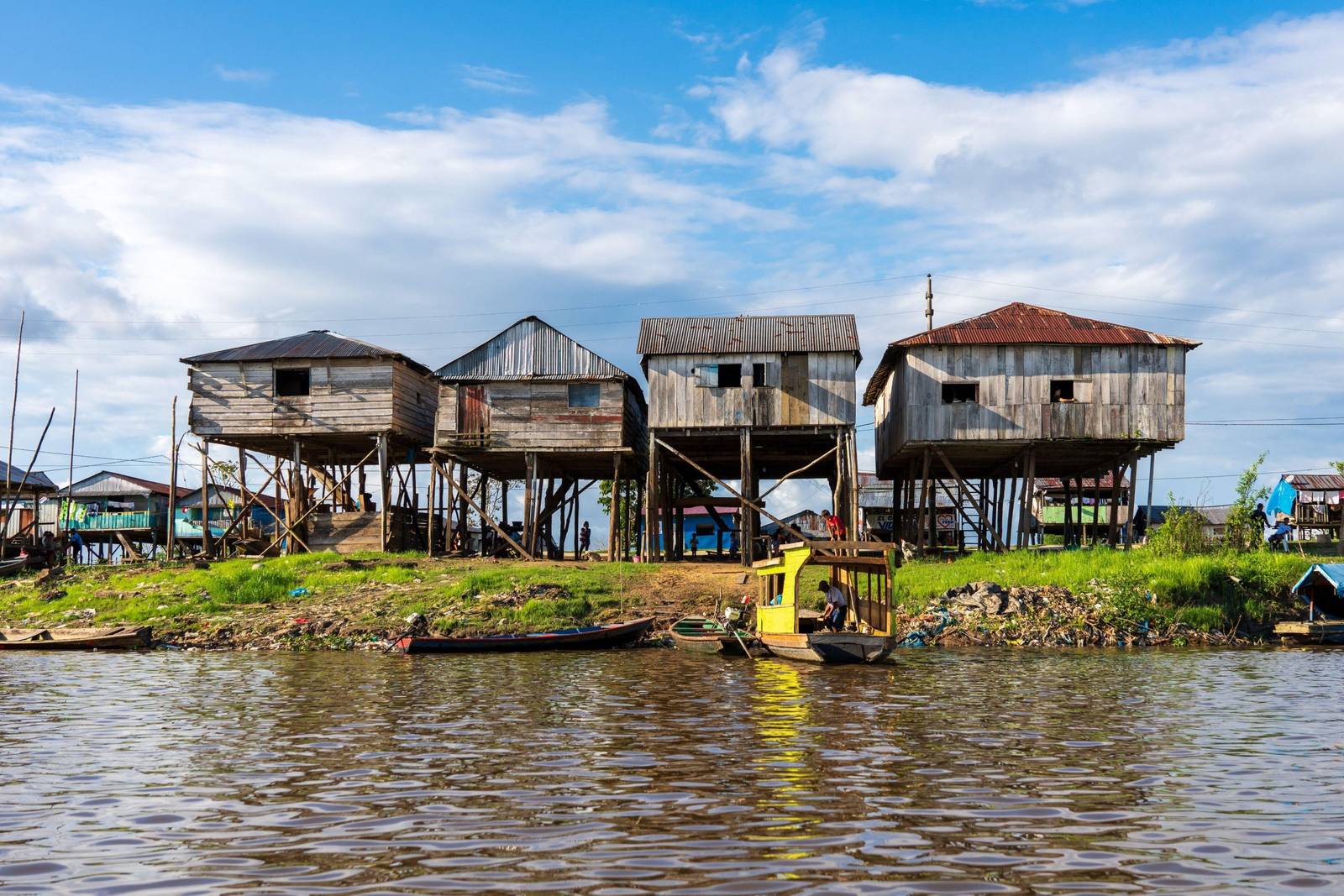 Viviendas palafíticas de madera a orillas de un río amazónico, con botes en primer plano