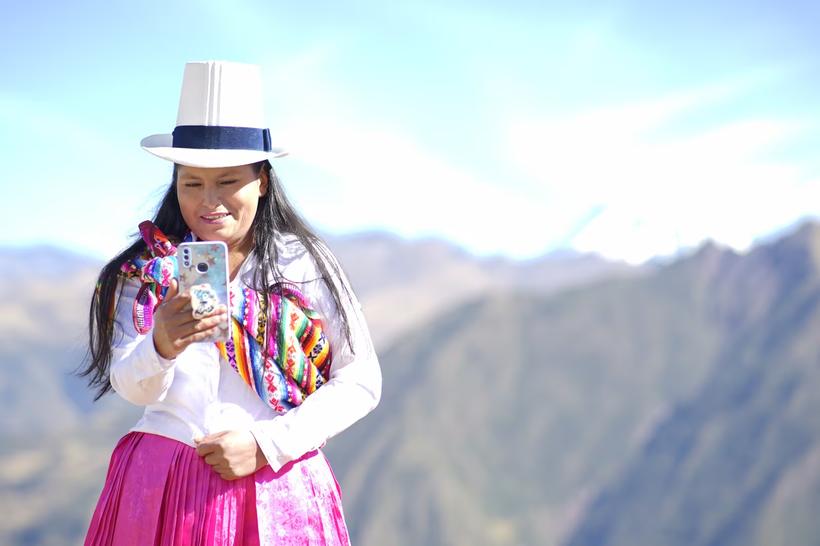 Mujer con vestimenta tradicional usando su celular en la sierra