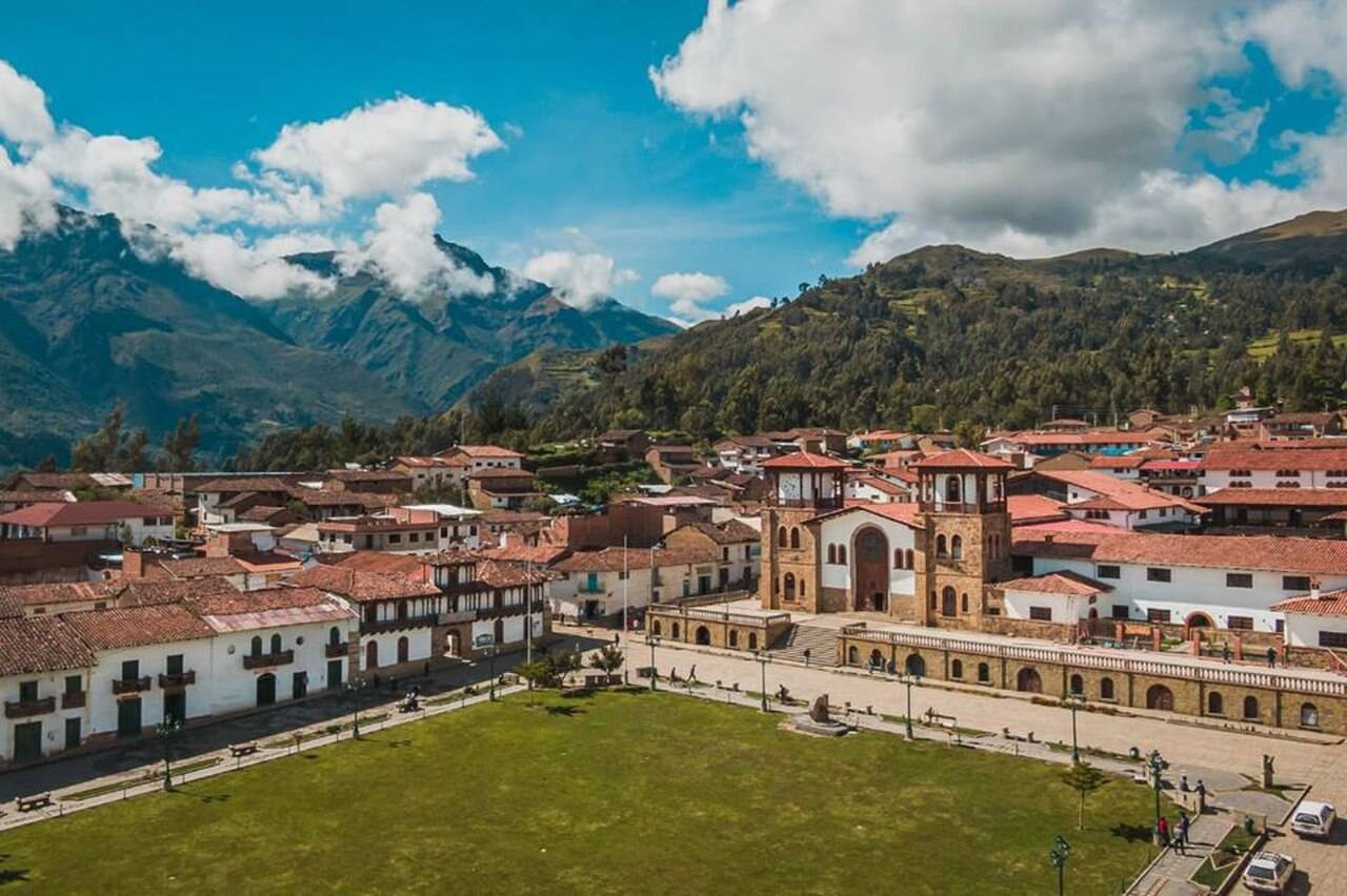 Plaza de un pueblo andino con iglesia de piedra, casas de techos de teja y montañas