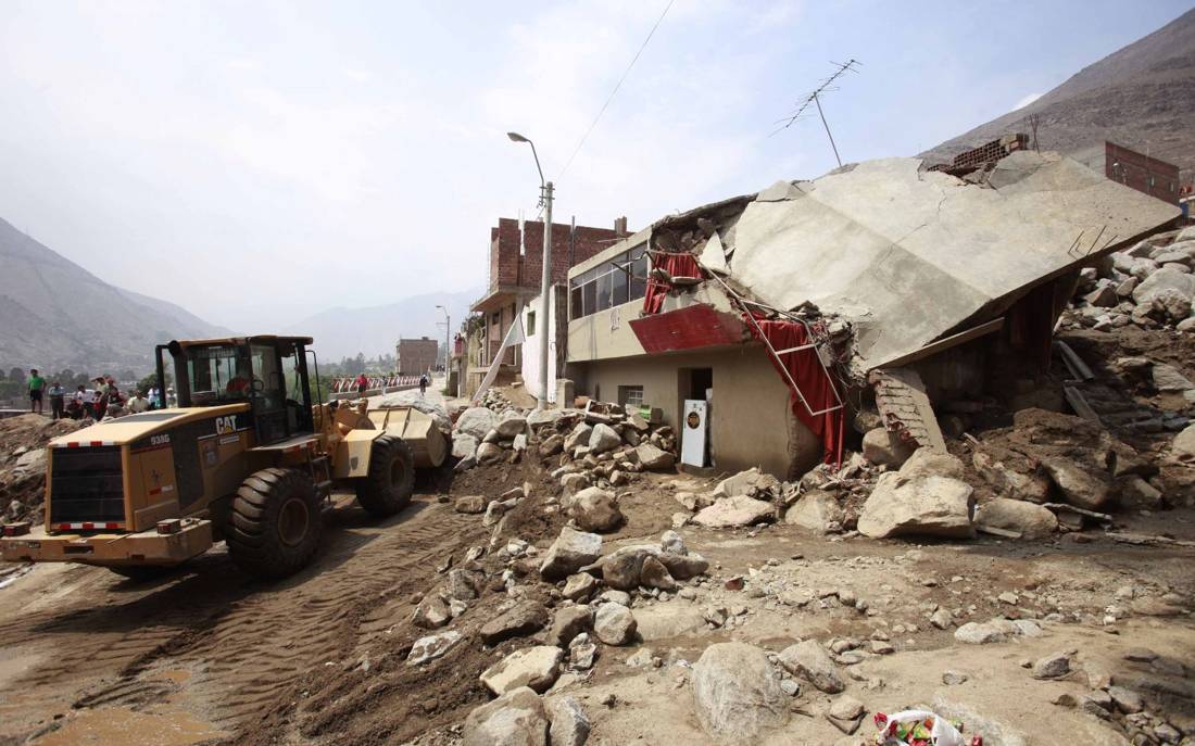 Maquinaria retirando escombros de un huaico junto a viviendas destruidas